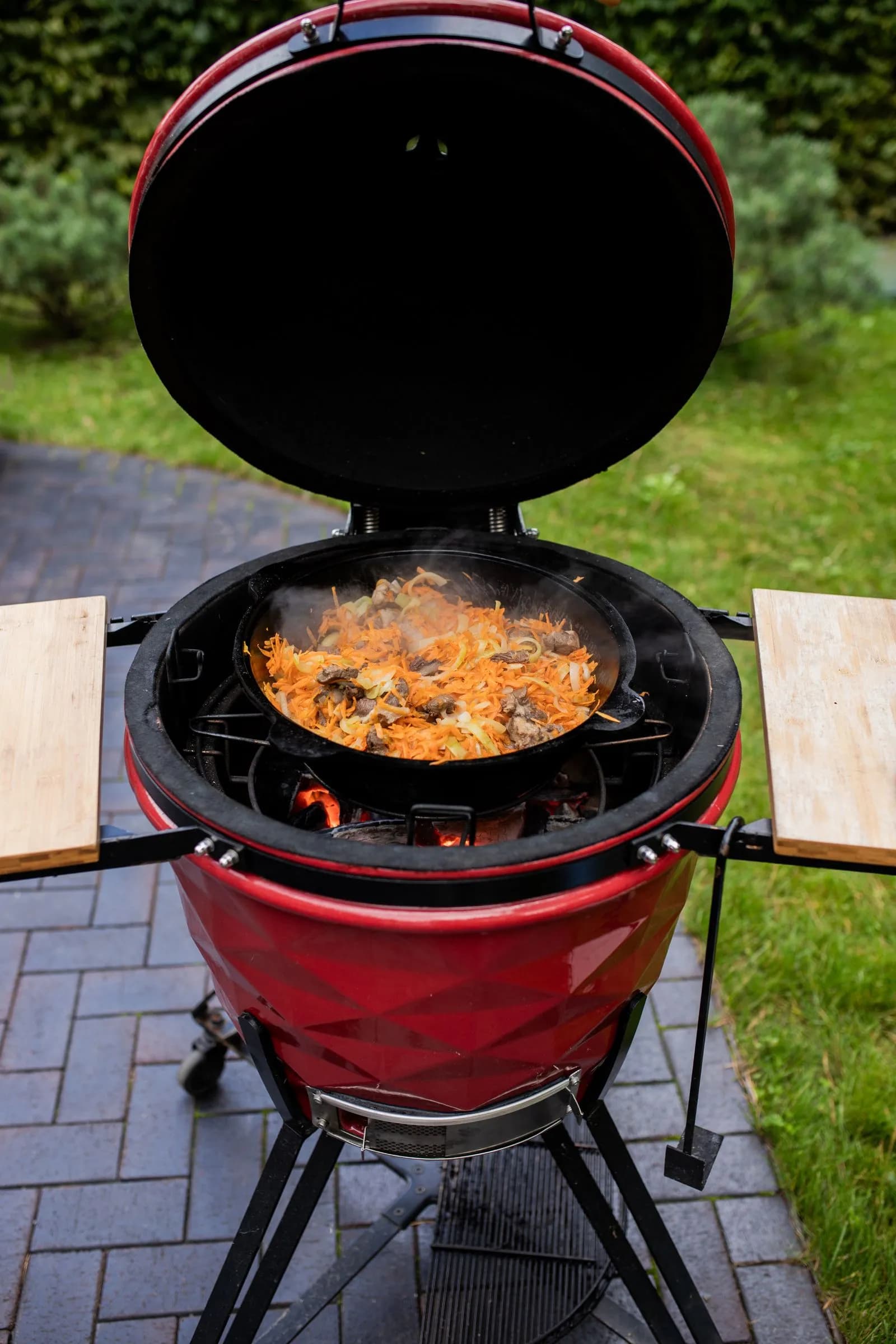 Kamado cerámico rojo abierto cocinando al aire libre en una terraza