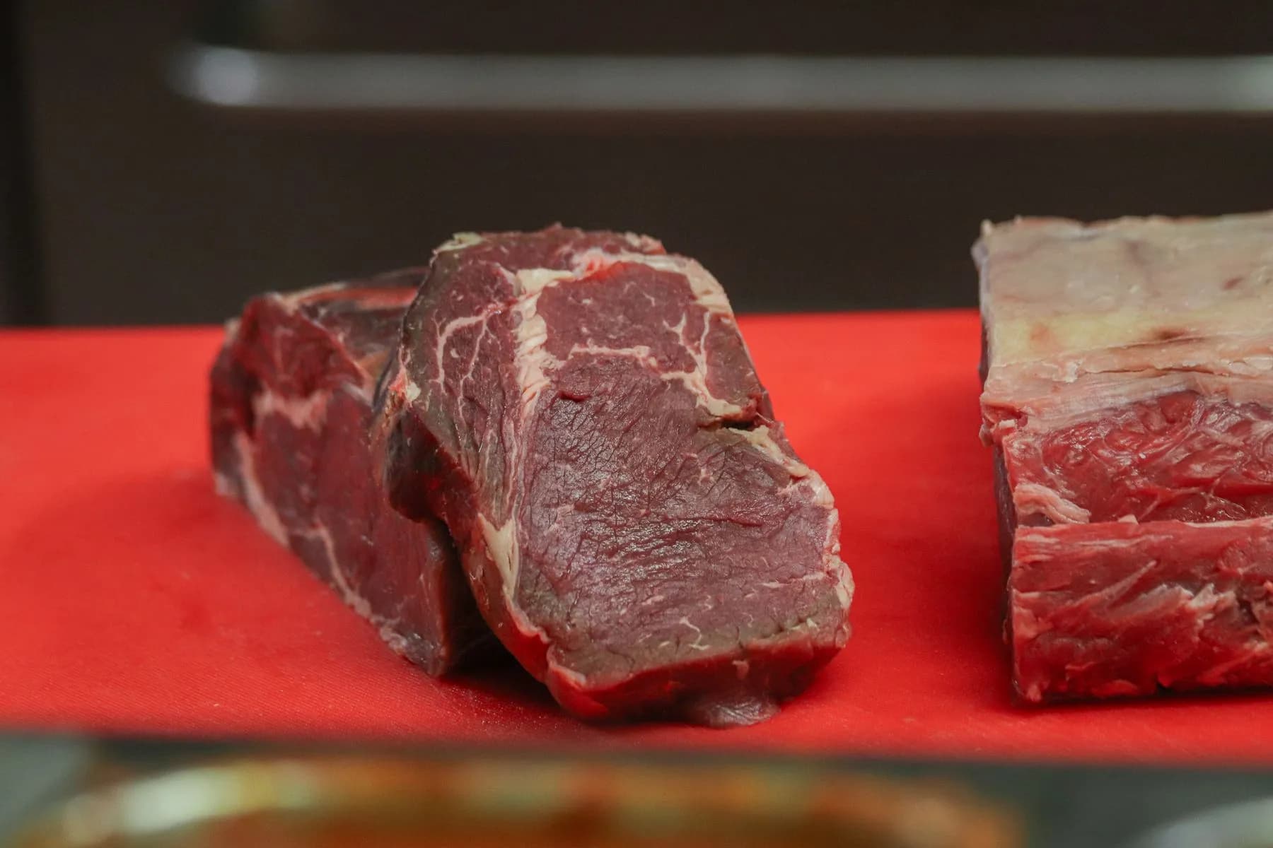 Piezas de vacuno crudas sobre una tabla roja de carnicería, con la grasa y el veteado a la vista