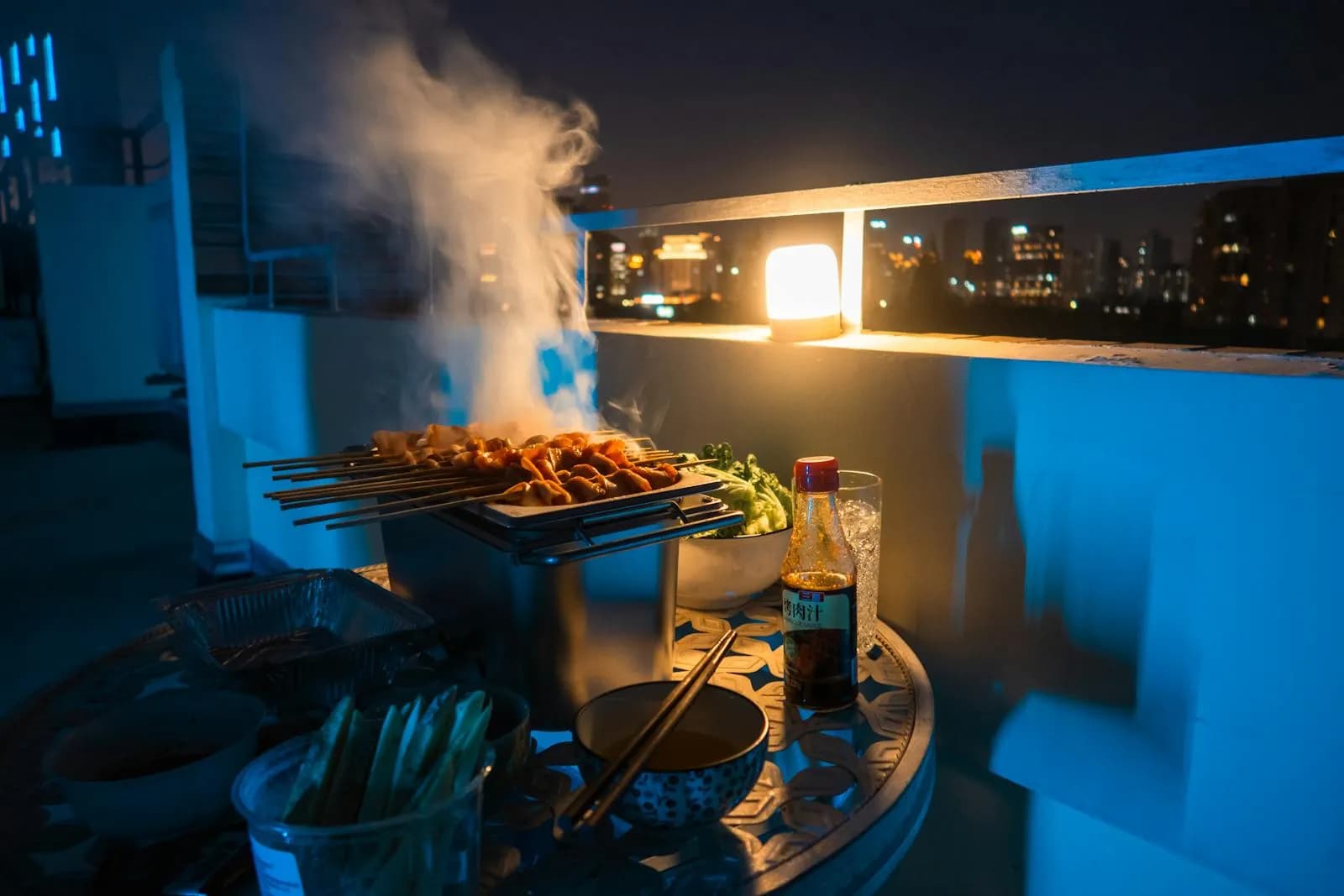 Barbacoa en una azotea urbana de noche con las luces de la ciudad al fondo