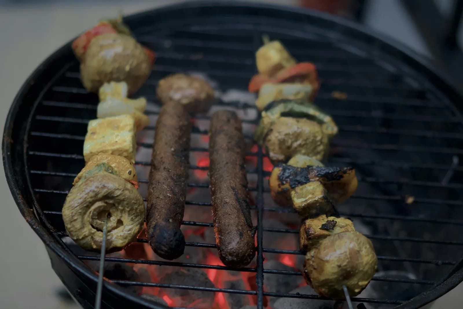 Brochetas y salchichas asándose sobre brasas en una barbacoa redonda pequeña de carbón, en un balcón
