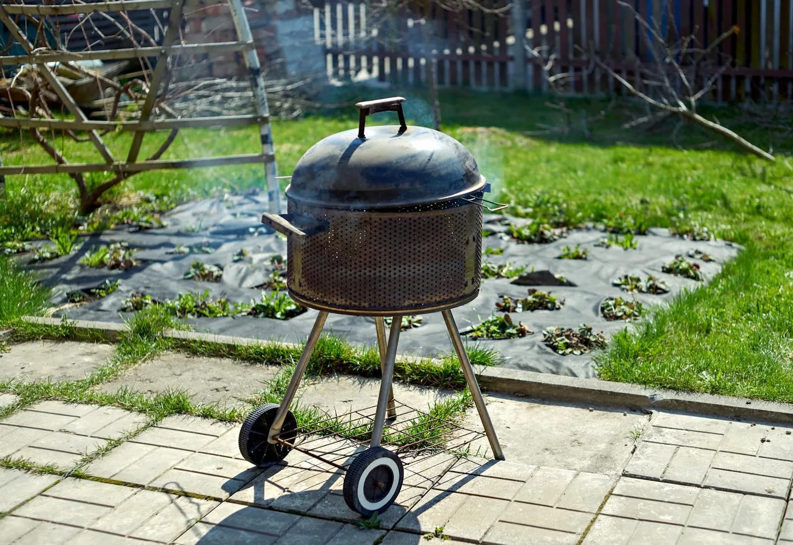 Barbacoa de carbón con tapa soltando humo en un jardín soleado