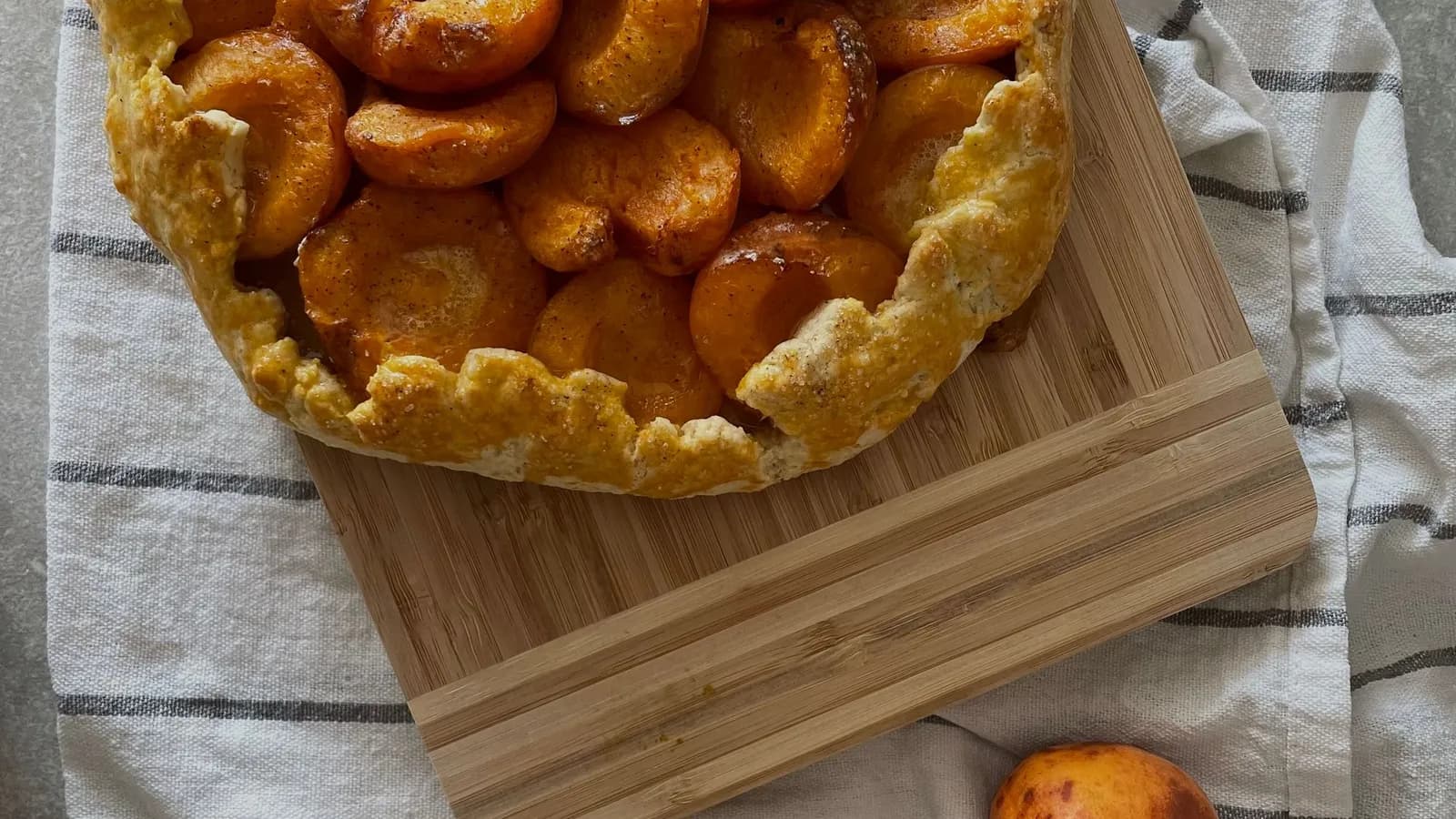 Galette rústica de albaricoques caramelizados con miel, recién horneada sobre tabla de madera, junto a albaricoques frescos.