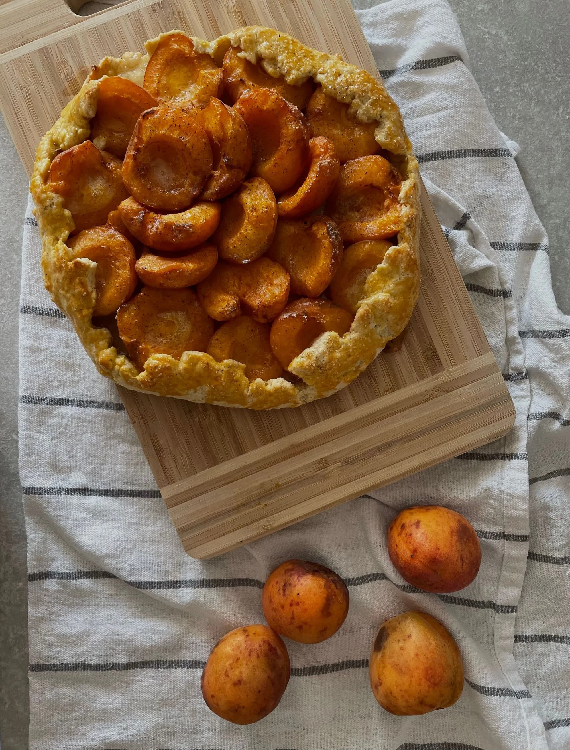 Galette rústica de albaricoques caramelizados con miel, recién horneada sobre tabla de madera, junto a albaricoques frescos.