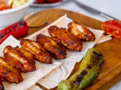 Alitas de pollo glaseadas y doradas sobre una tabla de madera con pimientos asados y guindilla