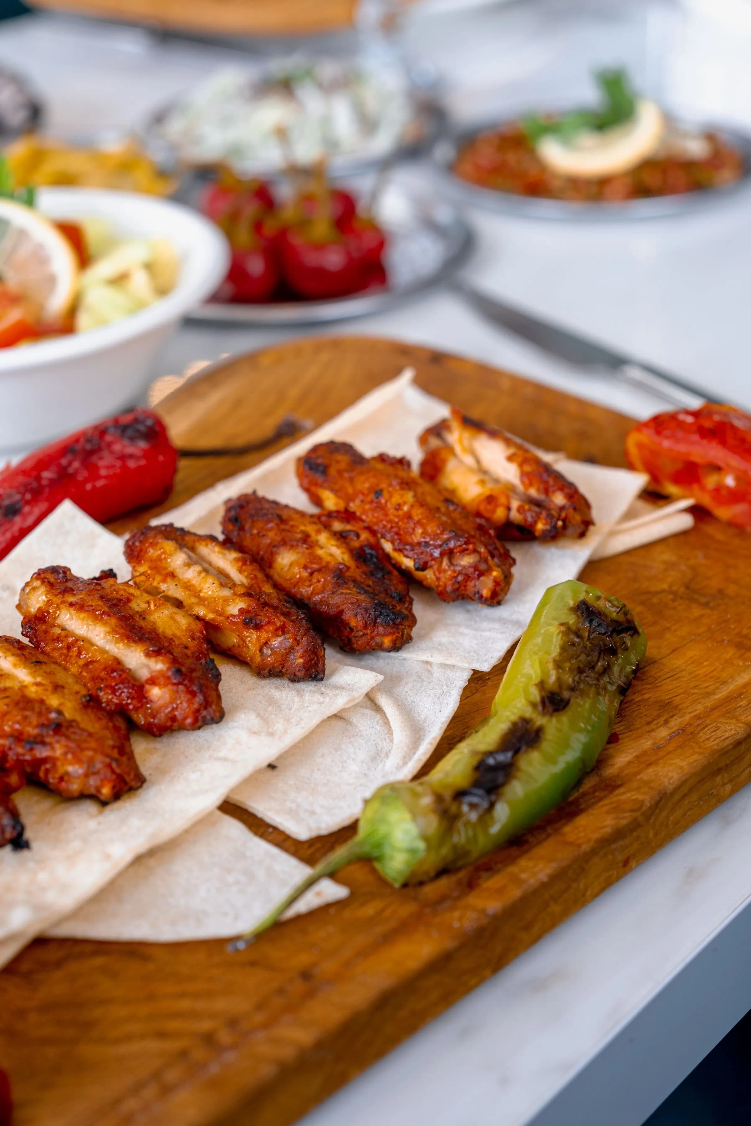 Alitas de pollo glaseadas y doradas sobre una tabla de madera con pimientos asados y guindilla