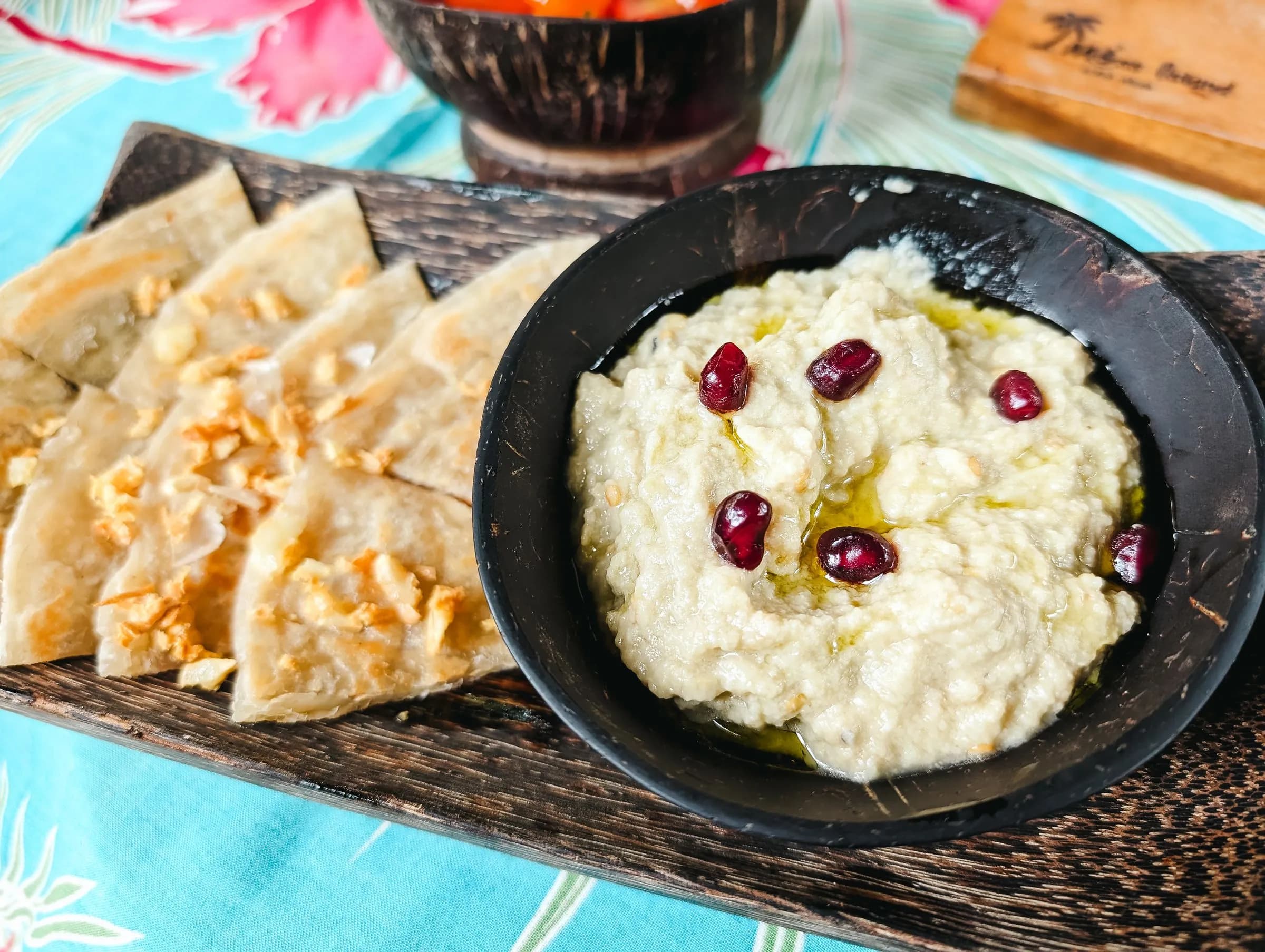 Cuenco de baba ganoush cremoso con granos de granada y aceite, junto a triángulos de pan de pita
