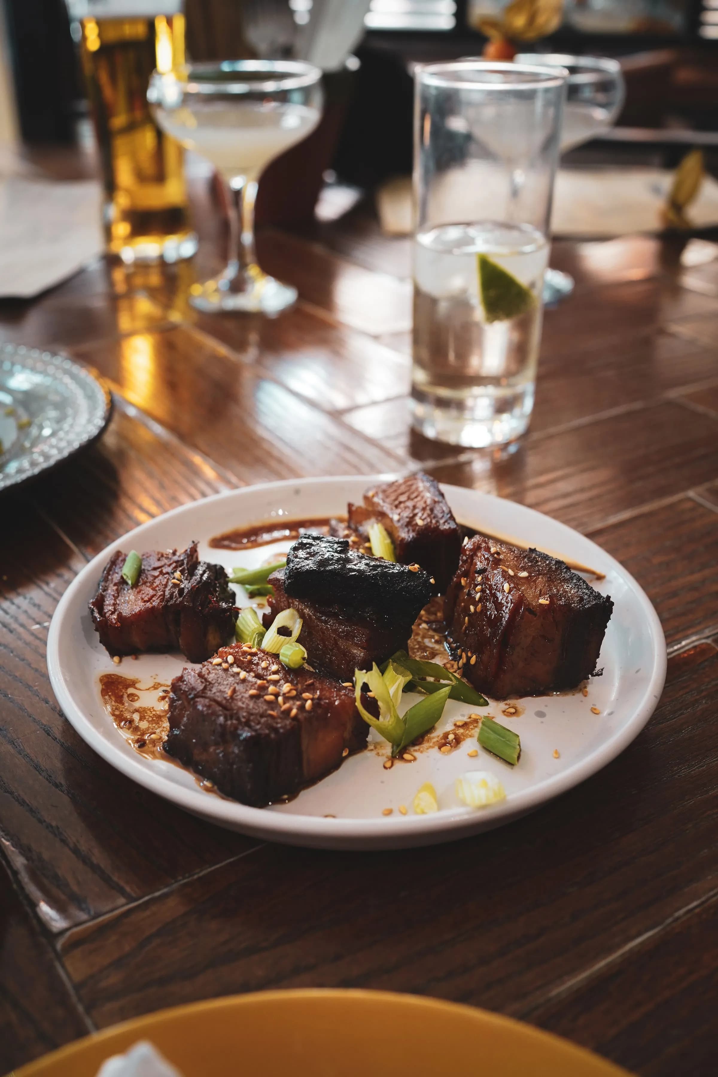 Dark, glazed cubes of pork belly with green leaves on a plate, on a wooden table