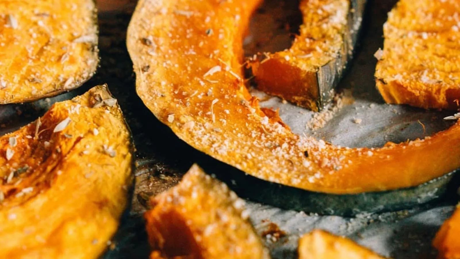 Gajos de calabaza asada con piel, caramelizados y espolvoreados con especias y sal sobre bandeja oscura