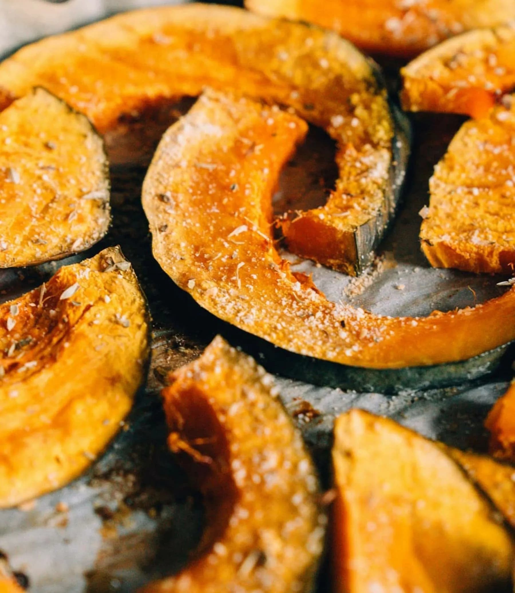 Gajos de calabaza asada con piel, caramelizados y espolvoreados con especias y sal sobre bandeja oscura