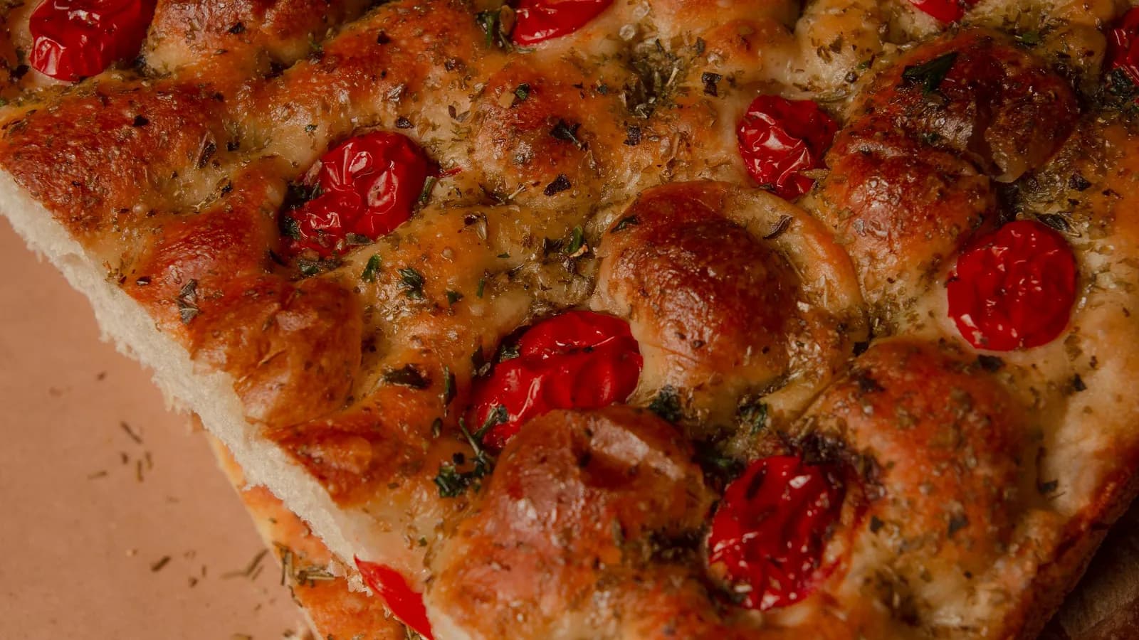 Coca dorada recién horneada con tomates cherry y hierbas frescas sobre papel kraft y romero