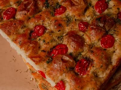 Coca dorada recién horneada con tomates cherry y hierbas frescas sobre papel kraft y romero