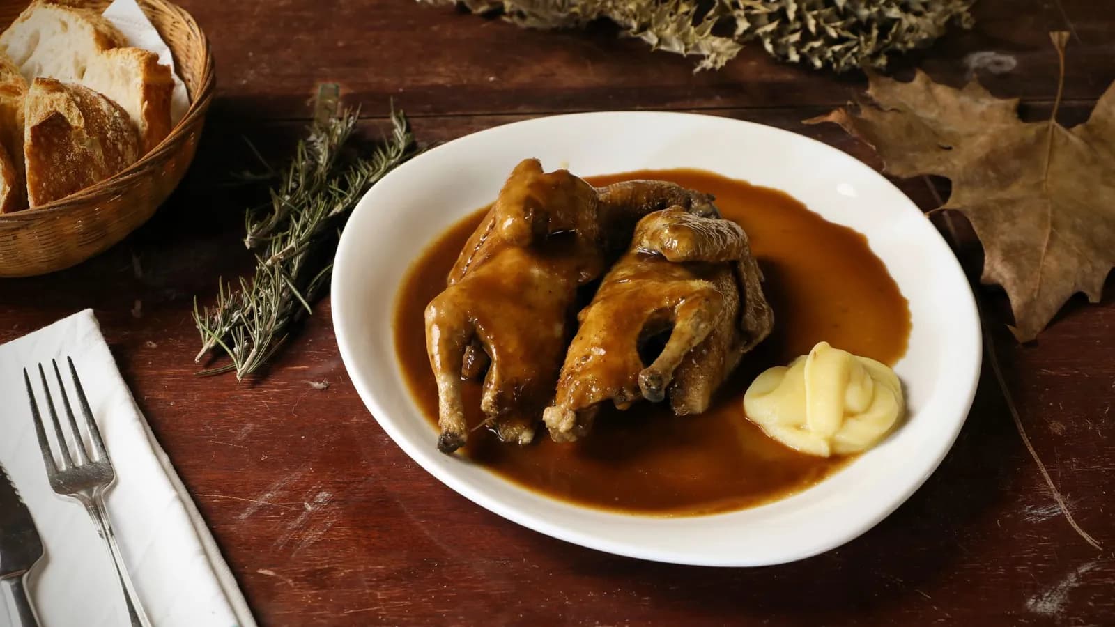 Codornices abiertas en mariposa y laqueadas con miel y romero, doradas sobre la parrilla de hierro fundido de un kamado cerámico humeante.