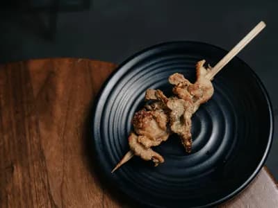 Codornices doradas con glaseado de miel en brocheta, presentadas sobre un plato oscuro, estilo editorial.