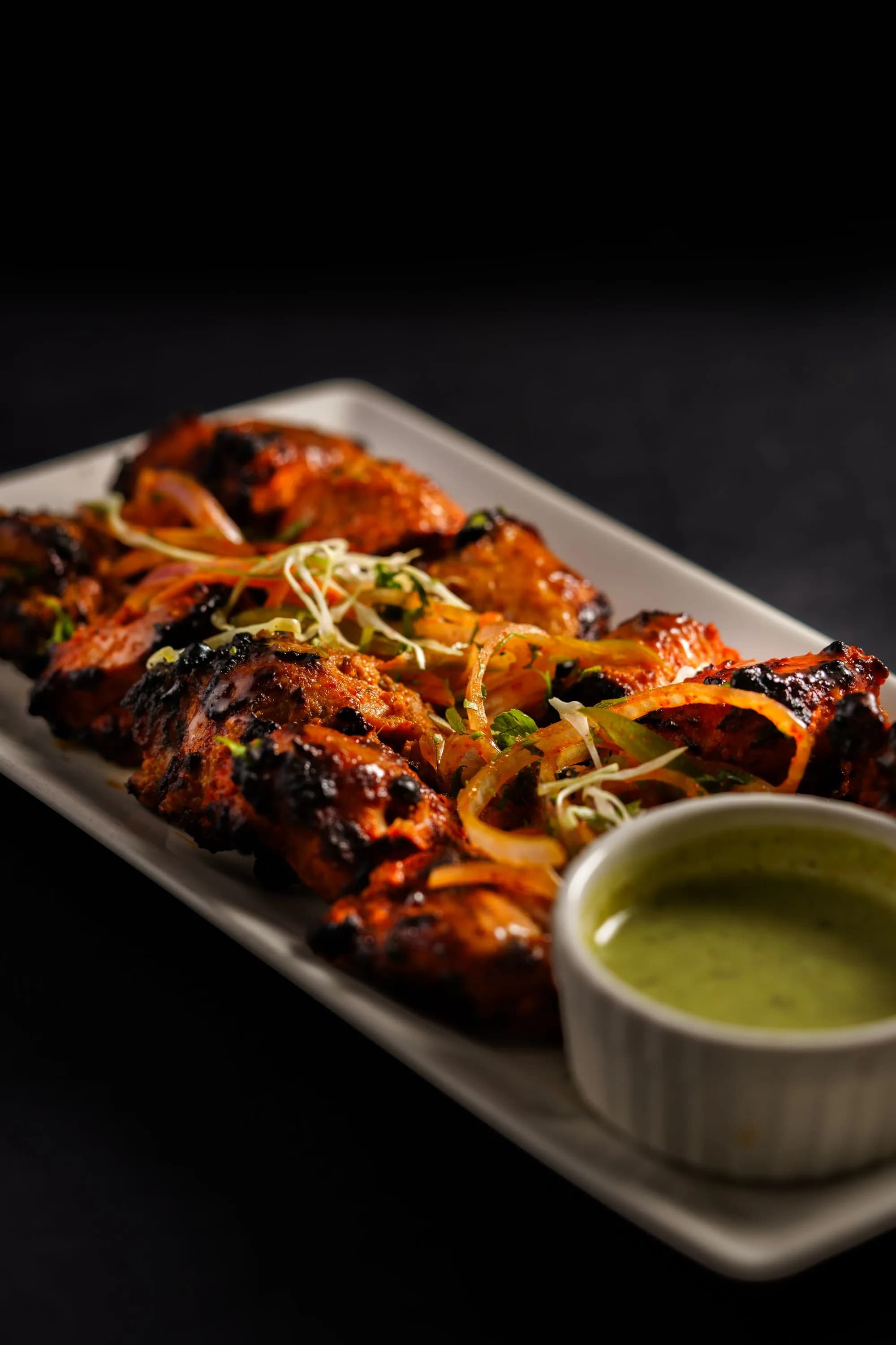 Contramuslos de pollo tandoori dorados y especiados sobre la parrilla de un kamado, junto a un cuenco de raita de pepino y gajos de lima.