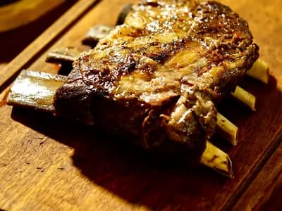 Costillar de vaca asado con la carne oscura sobre los huesos, en una tabla de madera