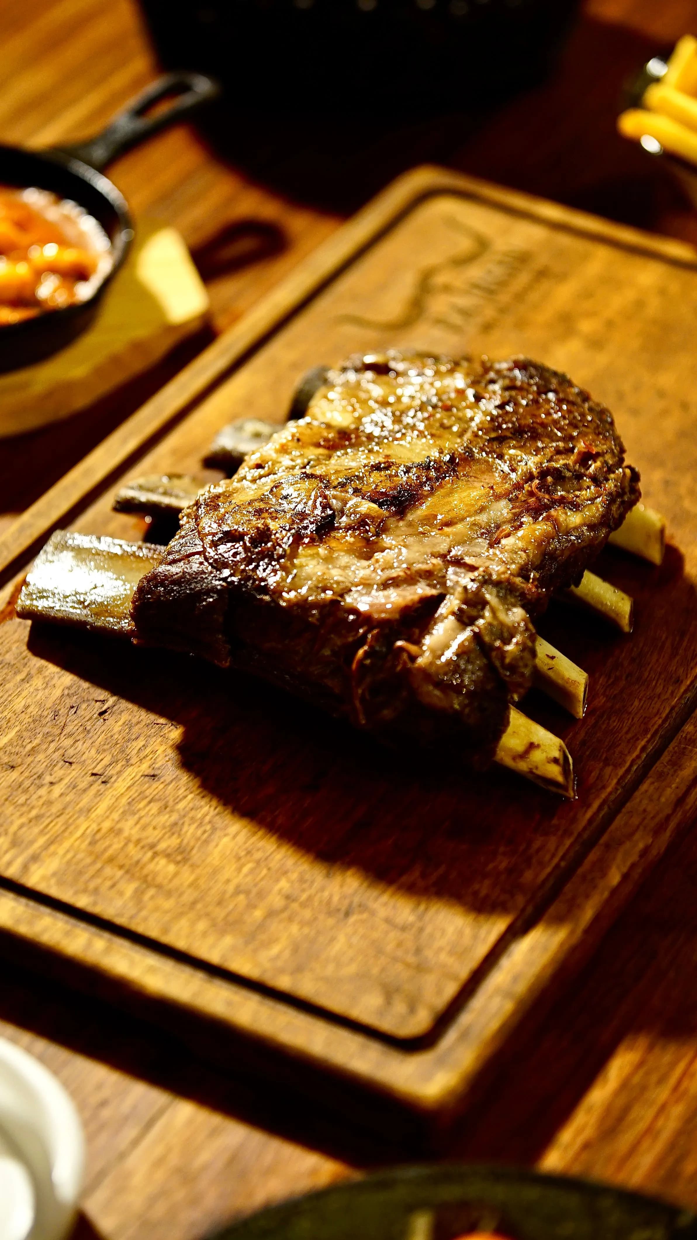 Costillar de vaca asado con la carne oscura sobre los huesos, en una tabla de madera