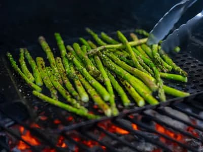 Espárragos trigueros marcados a la brasa sobre la rejilla de un kamado, con ralladura de limón y escamas de sal, algunos envueltos en jamón serrano.