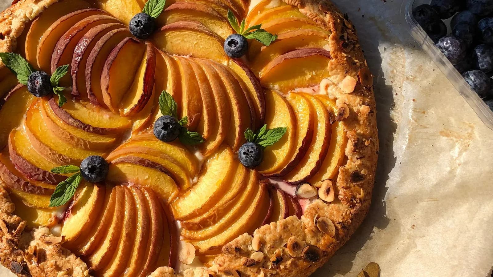 Galette rústica de nectarina y frambuesa recién horneada, con la masa quebrada dorada y la fruta caramelizada, sobre una piedra junto a un kamado de cerámica.