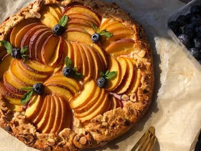 Galette rústica de nectarina y frambuesa recién horneada, con la masa quebrada dorada y la fruta caramelizada, sobre una piedra junto a un kamado de cerámica.