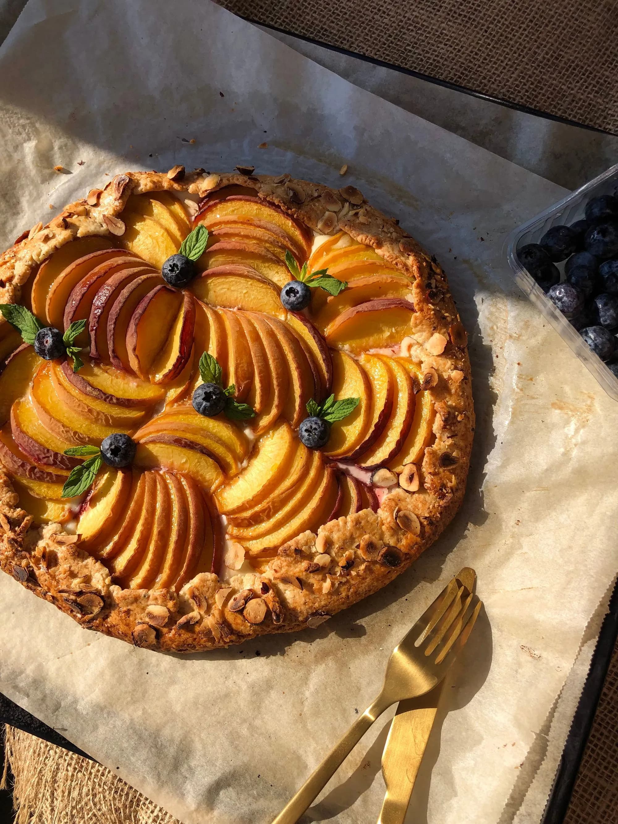 Galette rústica de nectarina y frambuesa recién horneada, con la masa quebrada dorada y la fruta caramelizada, sobre una piedra junto a un kamado de cerámica.