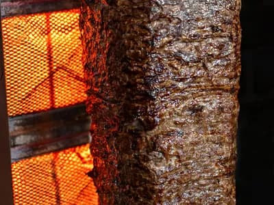 Bloque de gyros girando en el asador vertical, con la cara exterior tostada lista para cortar