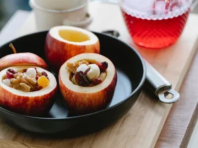 Manzanas rojas rellenas de frutos secos en una sartén negra, junto a una jarra de almíbar