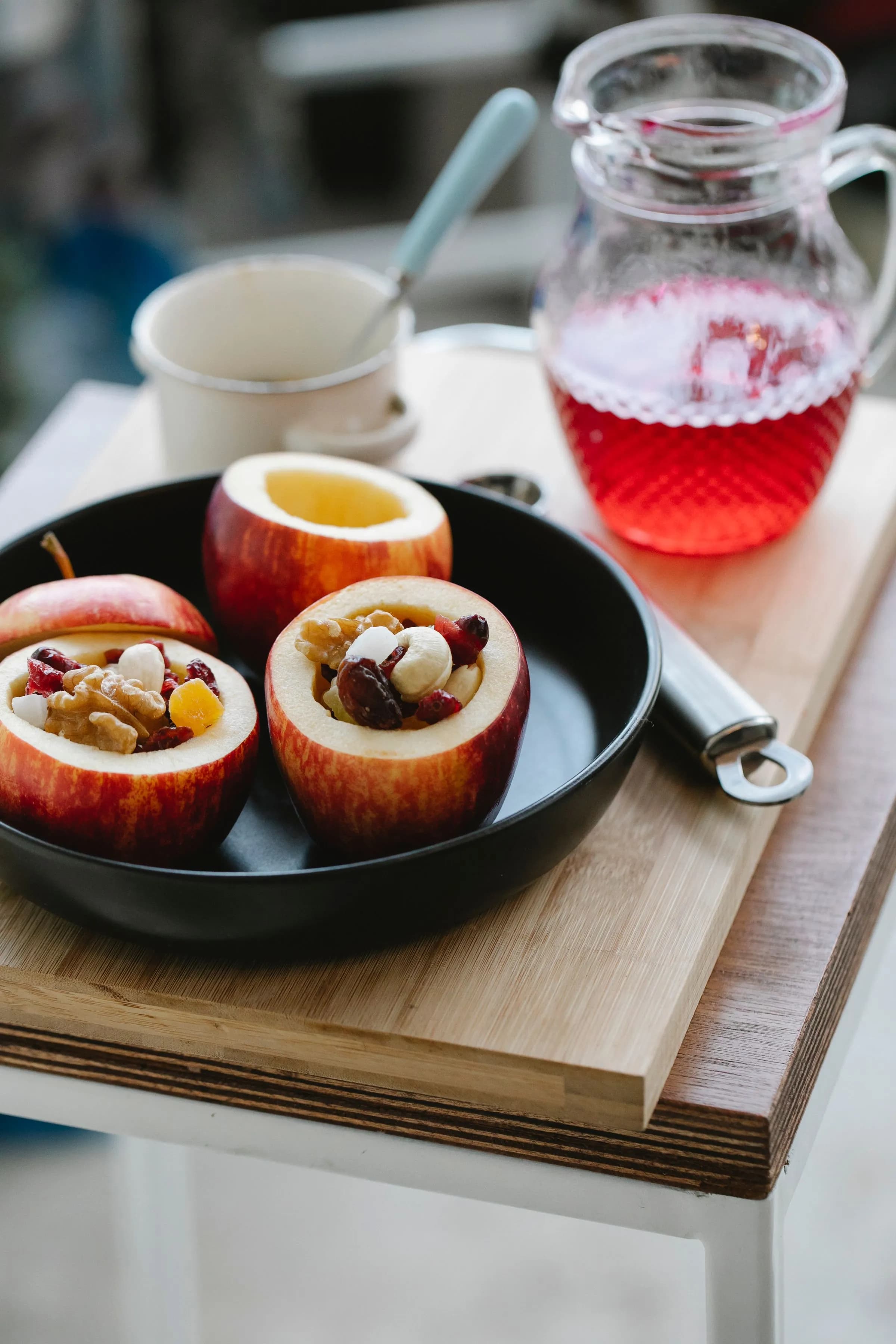 Manzanas rojas rellenas de frutos secos en una sartén negra, junto a una jarra de almíbar