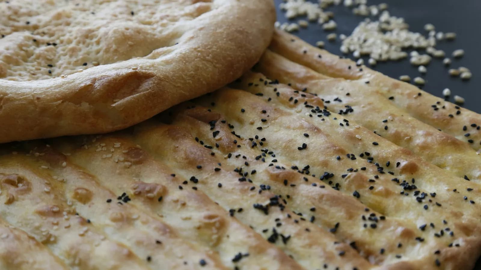 Naan recién horneado y ampollado, pincelado con mantequilla de ajo y espolvoreado con cilantro, sobre una piedra junto a un kamado de cerámica.
