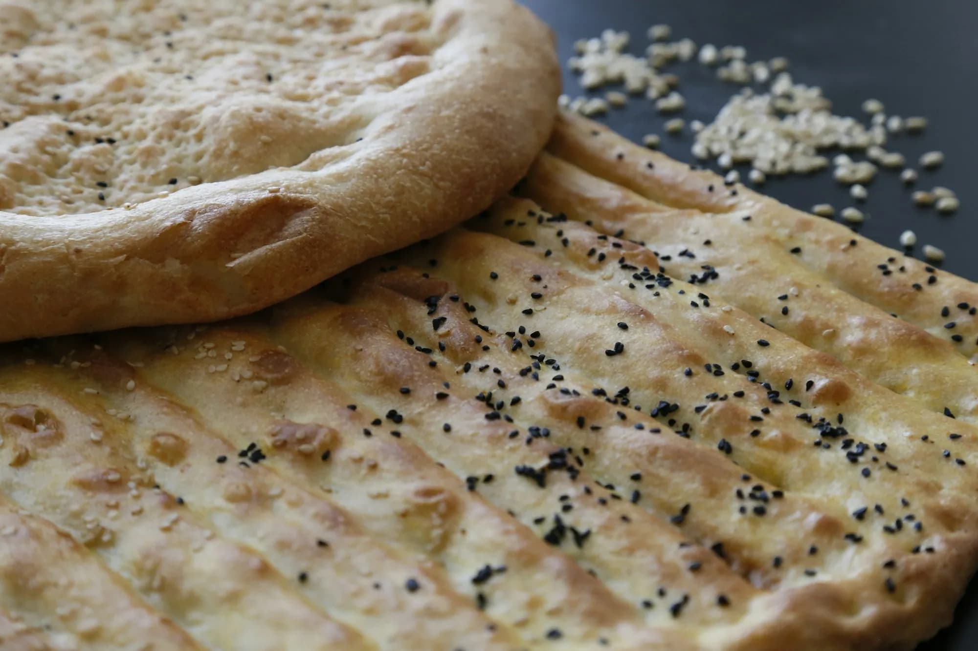 Naan recién horneado y ampollado, pincelado con mantequilla de ajo y espolvoreado con cilantro, sobre una piedra junto a un kamado de cerámica.
