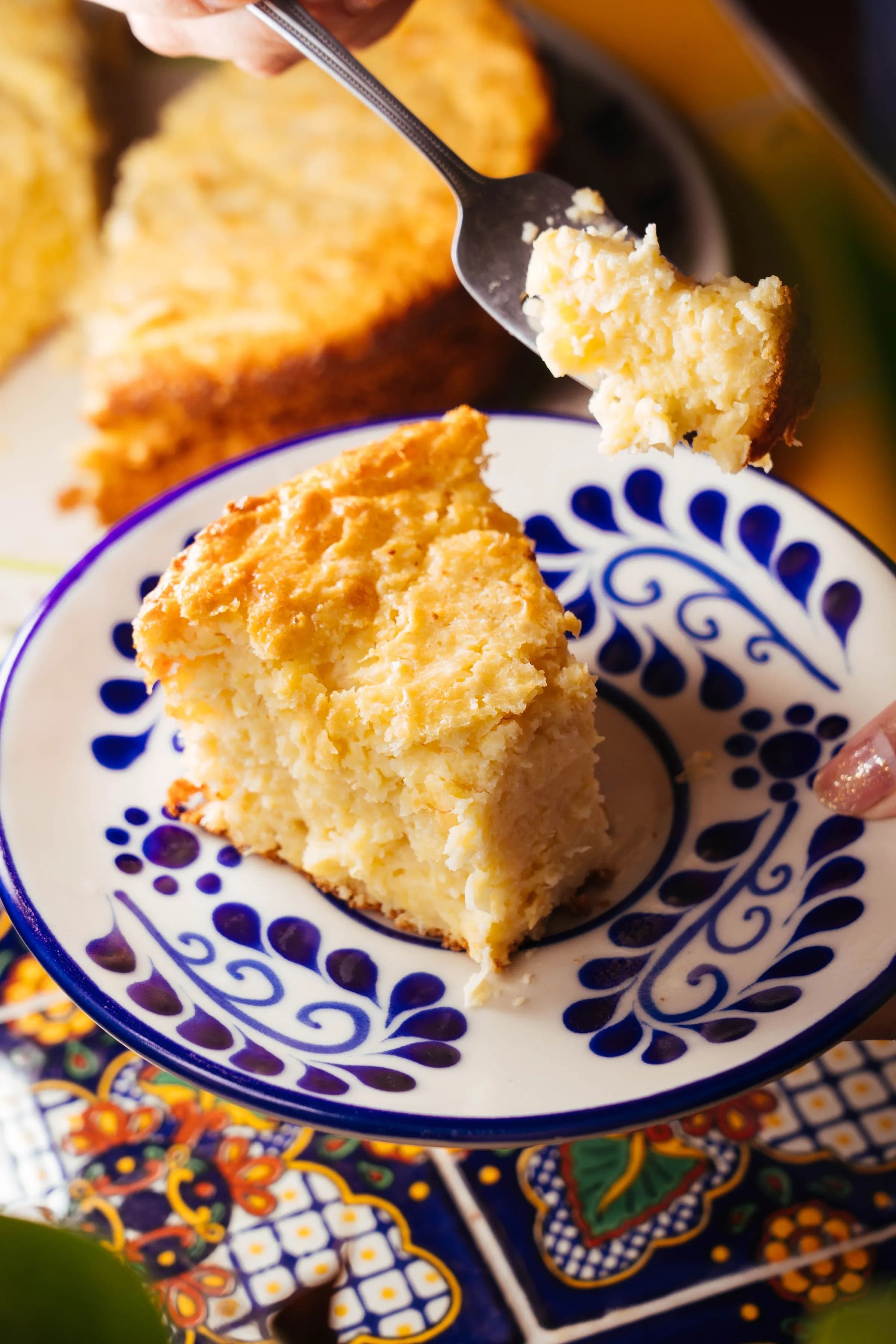 Porción de pan de maíz dorado en un plato de cerámica azul y blanca, con una cuchara cogiendo un trozo
