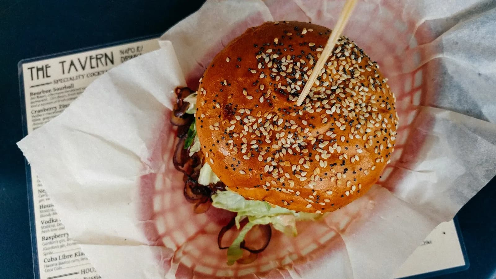 Bollos de hamburguesa brioche recién horneados, dorados y brillantes con sésamo, enfriándose sobre una rejilla junto a un kamado de cerámica.