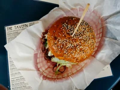 Bollos de hamburguesa brioche recién horneados, dorados y brillantes con sésamo, enfriándose sobre una rejilla junto a un kamado de cerámica.