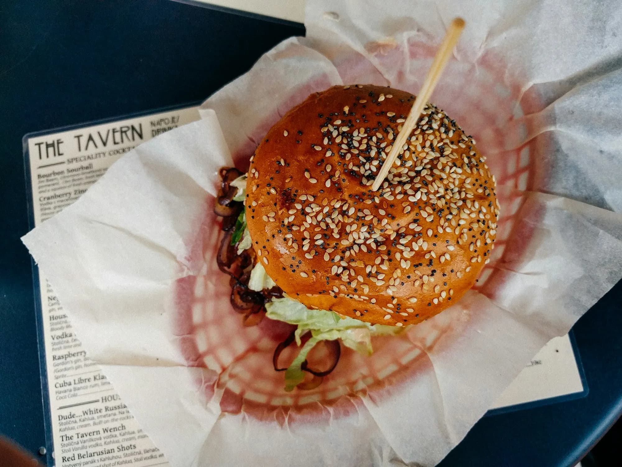 Bollos de hamburguesa brioche recién horneados, dorados y brillantes con sésamo, enfriándose sobre una rejilla junto a un kamado de cerámica.
