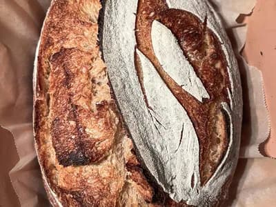 Hogaza de masa madre dorada saliendo de una cocotte de hierro fundido