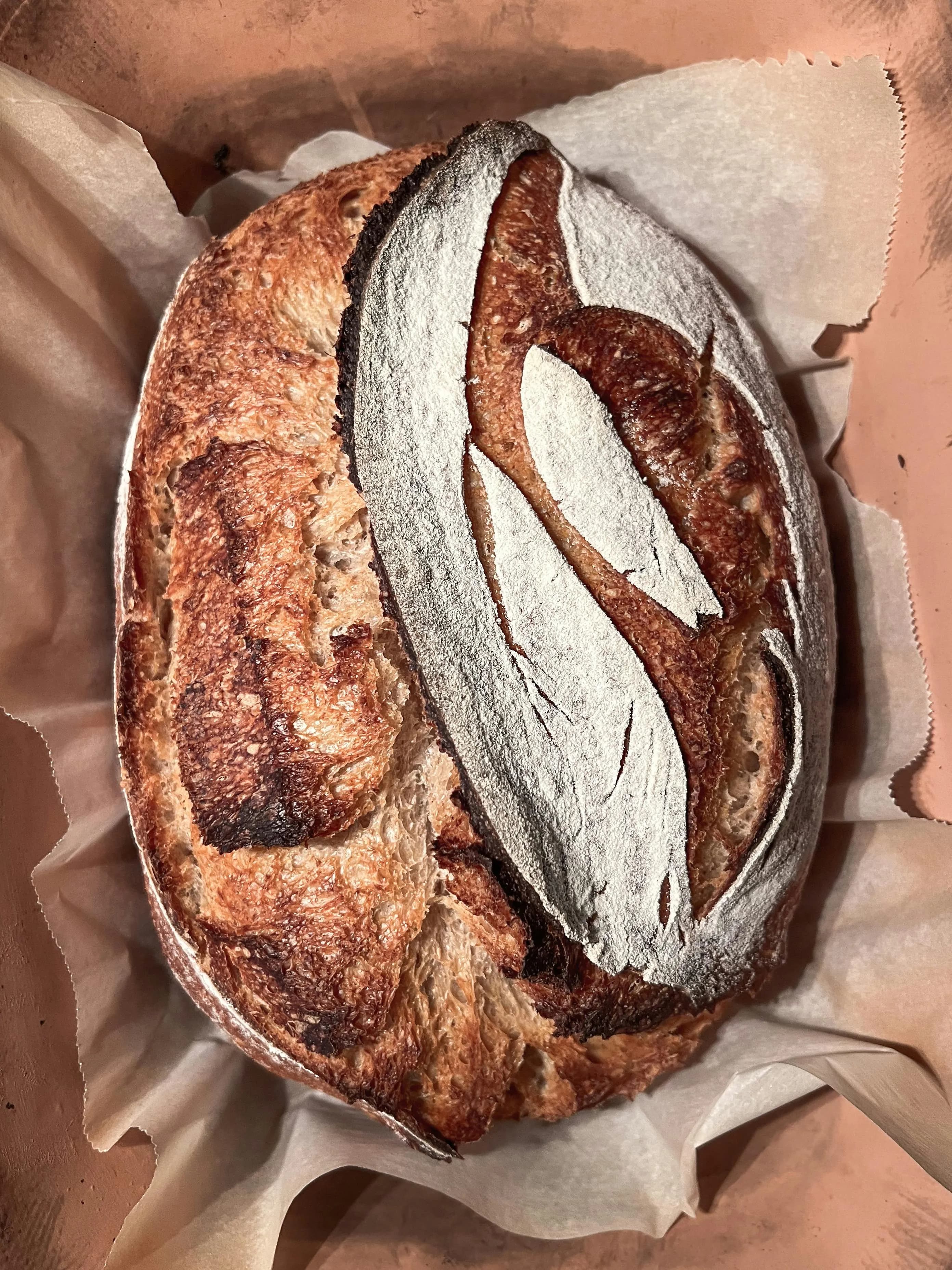 Hogaza de masa madre dorada saliendo de una cocotte de hierro fundido