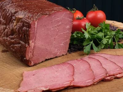 Pieza de pastrami ahumado con corteza oscura y lonchas rosadas sobre tabla de madera