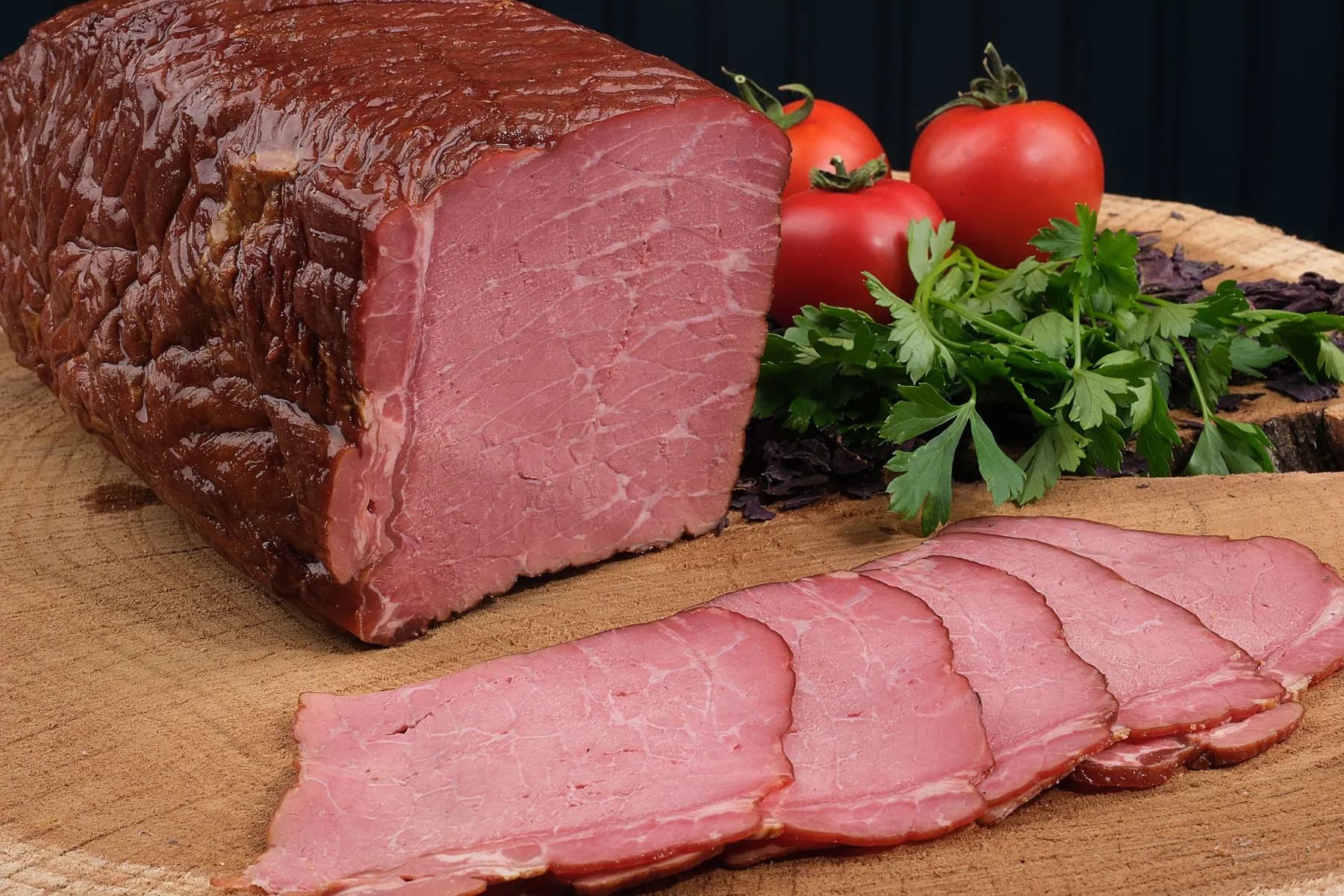 Pieza de pastrami ahumado con corteza oscura y lonchas rosadas sobre tabla de madera