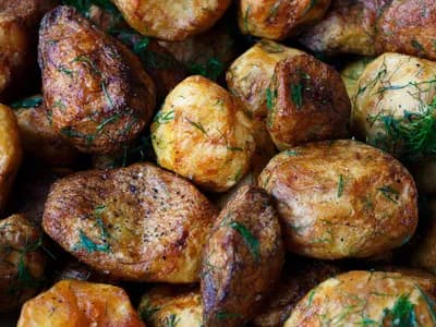 Primer plano de patatas asadas de piel dorada y tostada, espolvoreadas con romero picado y pimienta negra