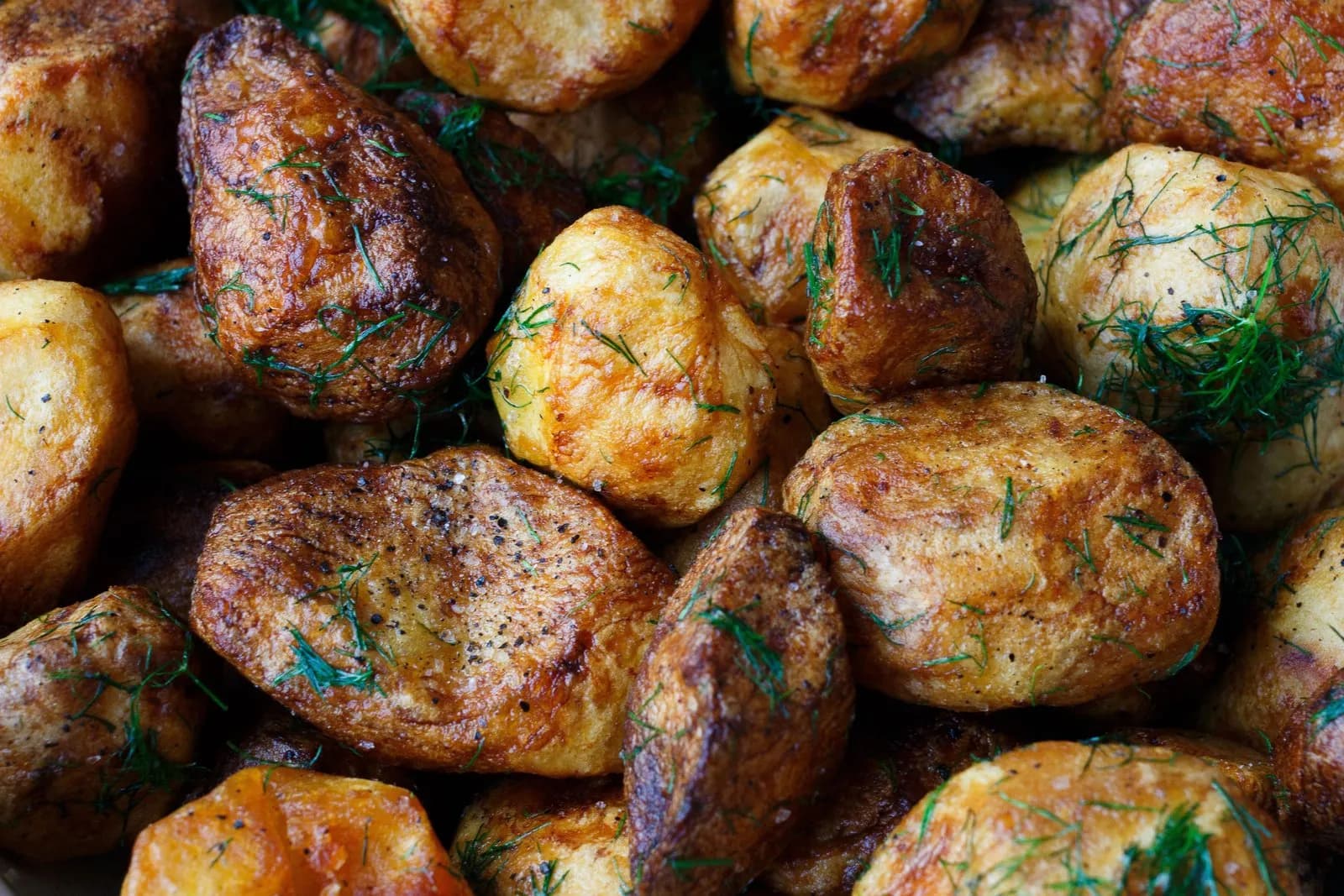 Primer plano de patatas asadas de piel dorada y tostada, espolvoreadas con romero picado y pimienta negra