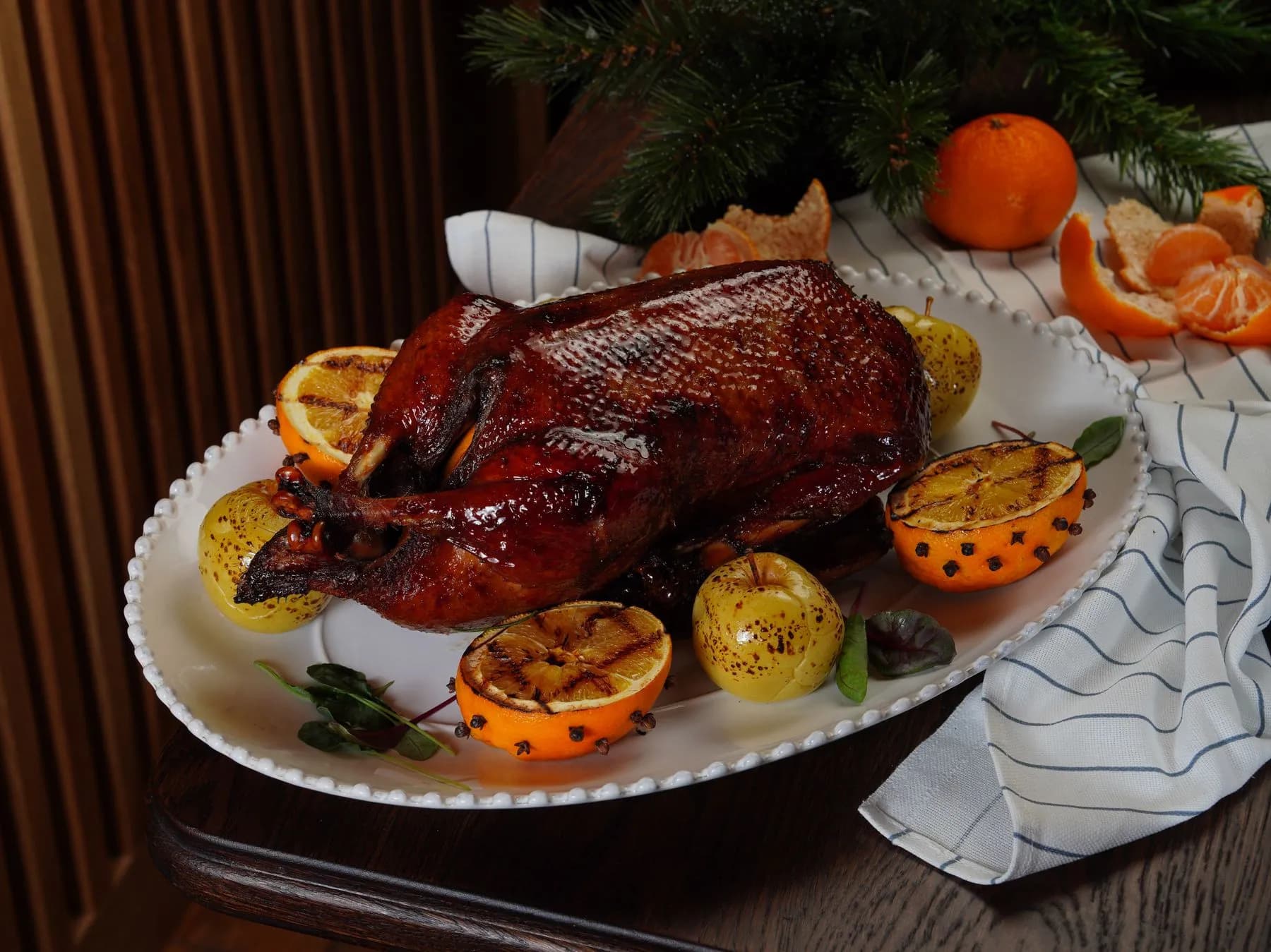 Pato entero asado con piel lacada, manzanas asadas y medias naranjas a la parrilla con clavo