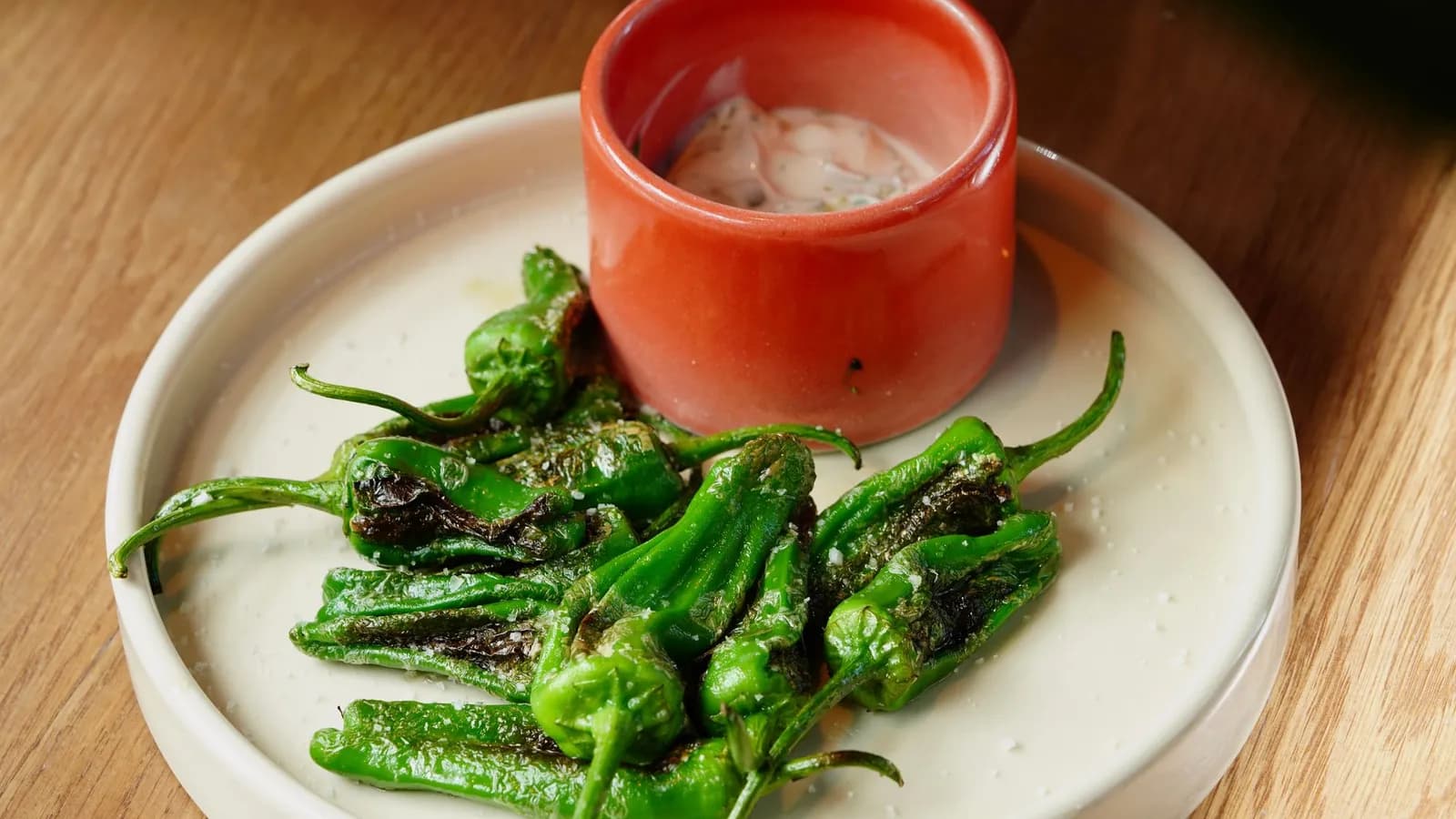 Pimientos de Padrón brillantes de aceite y con la piel ampollada, recién salteados en una sartén de hierro sobre un kamado, espolvoreados con sal en escamas.