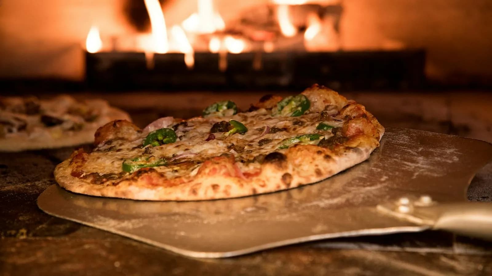 Pizza de masa madre con corteza leopardada saliendo del horno de leña