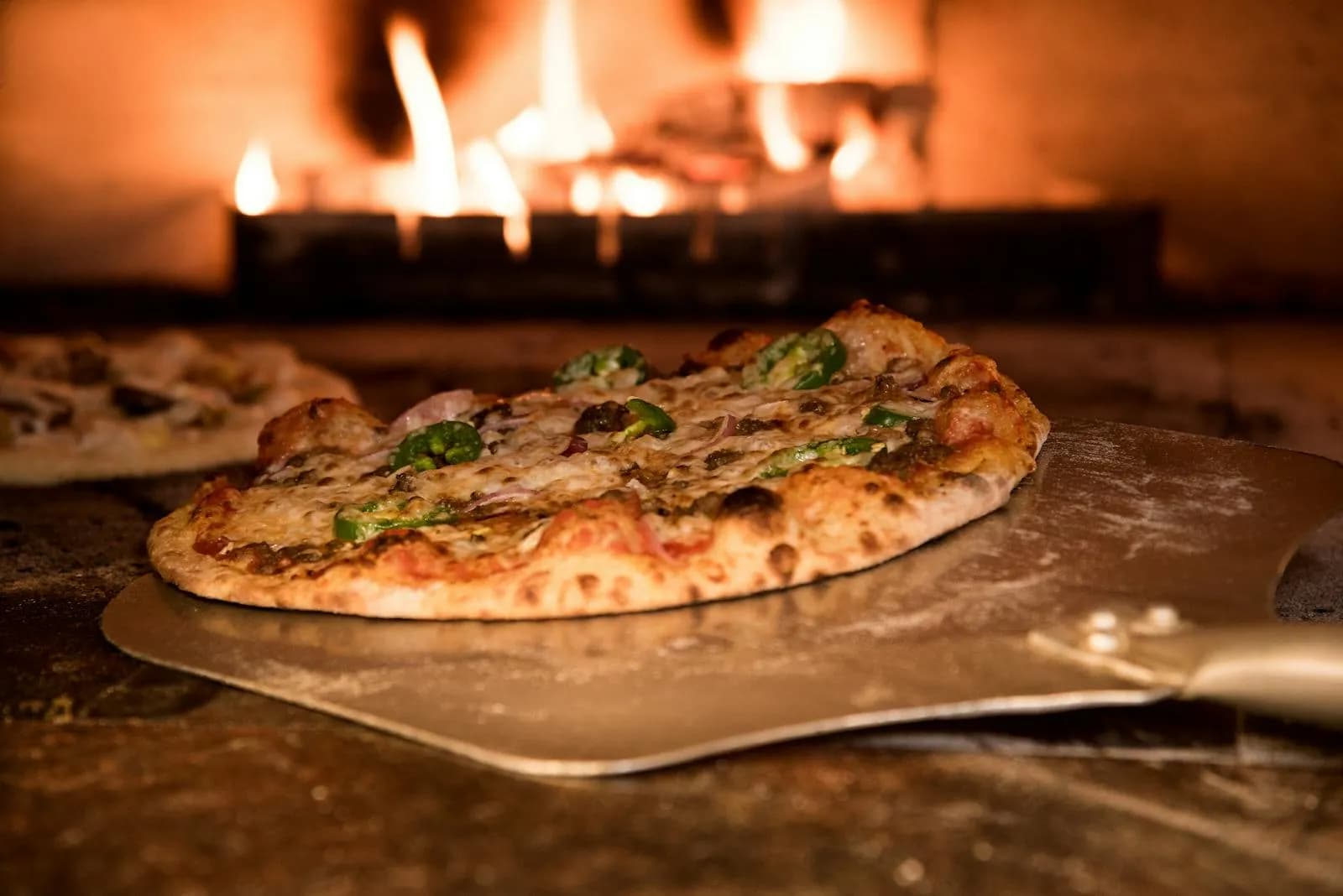 Pizza de masa madre con corteza leopardada saliendo del horno de leña