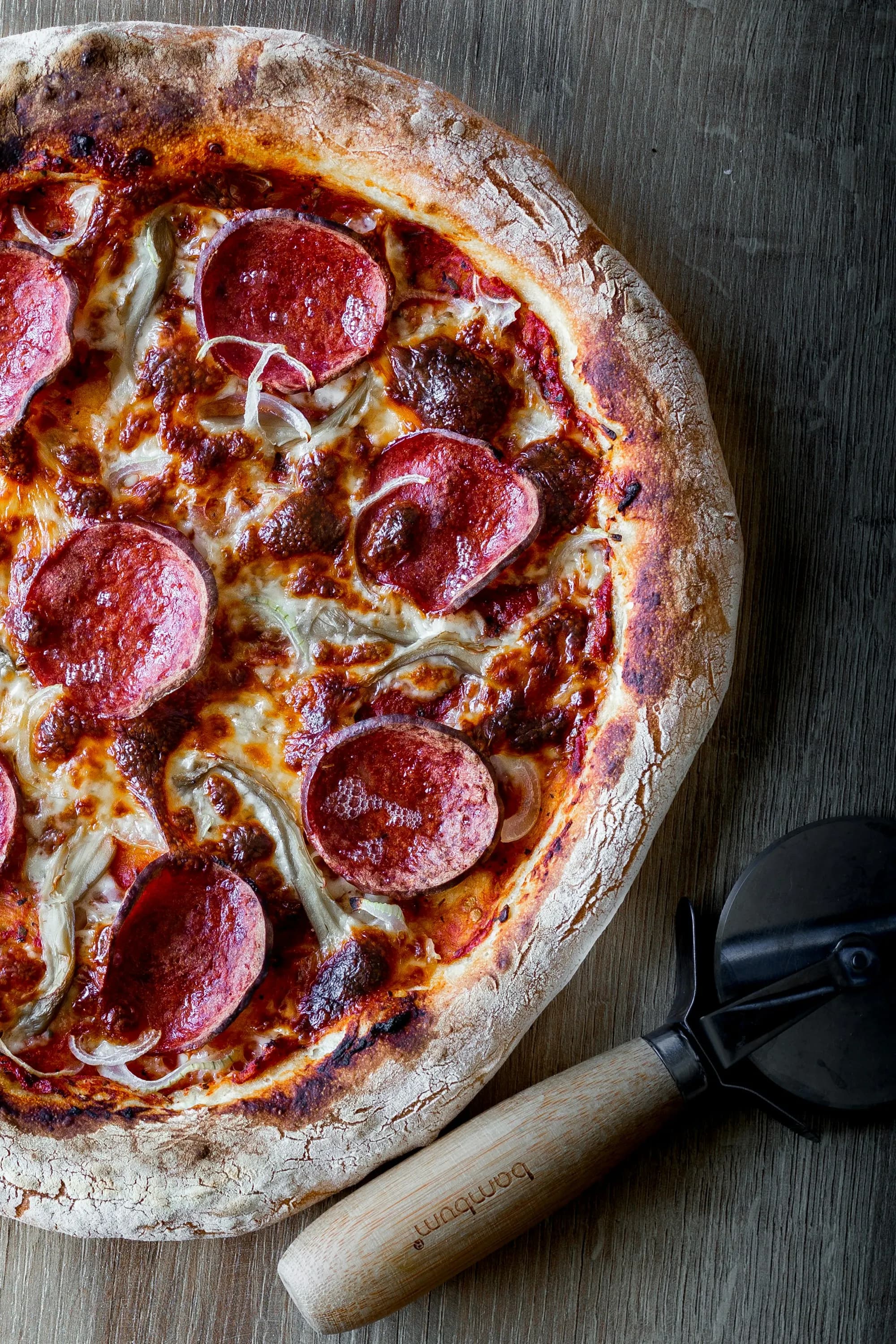 Pizza diavola con salami picante y cebolla roja, borde carbonizado de horno de leña