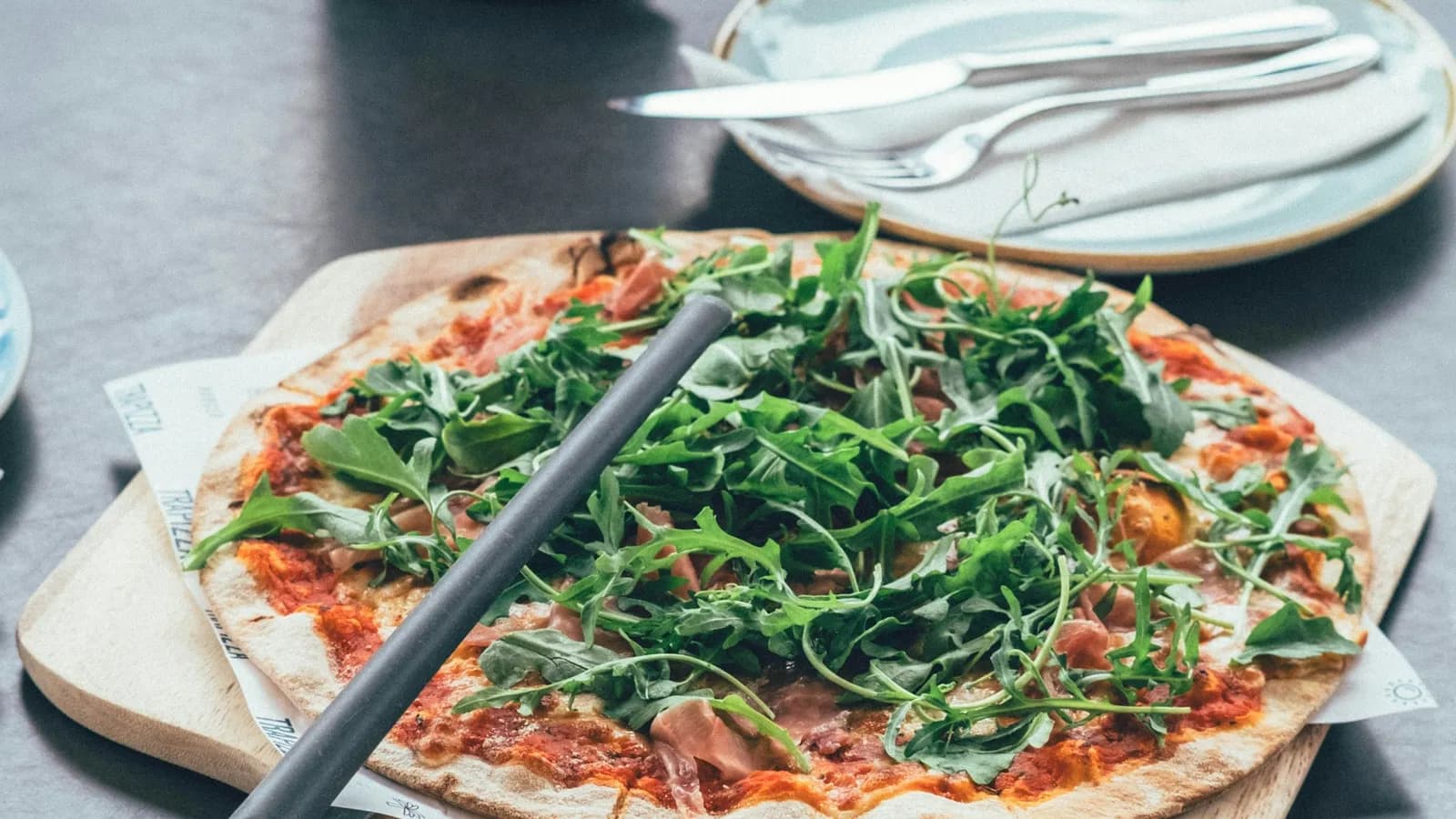 Pizza de jamón y rúcula fresca servida sobre pala de madera