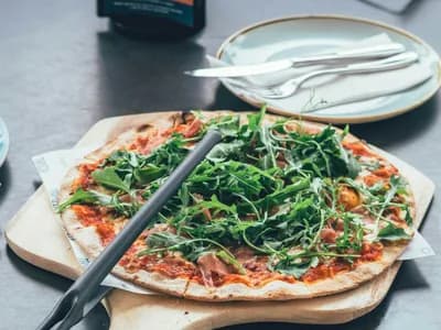 Pizza de jamón y rúcula fresca servida sobre pala de madera