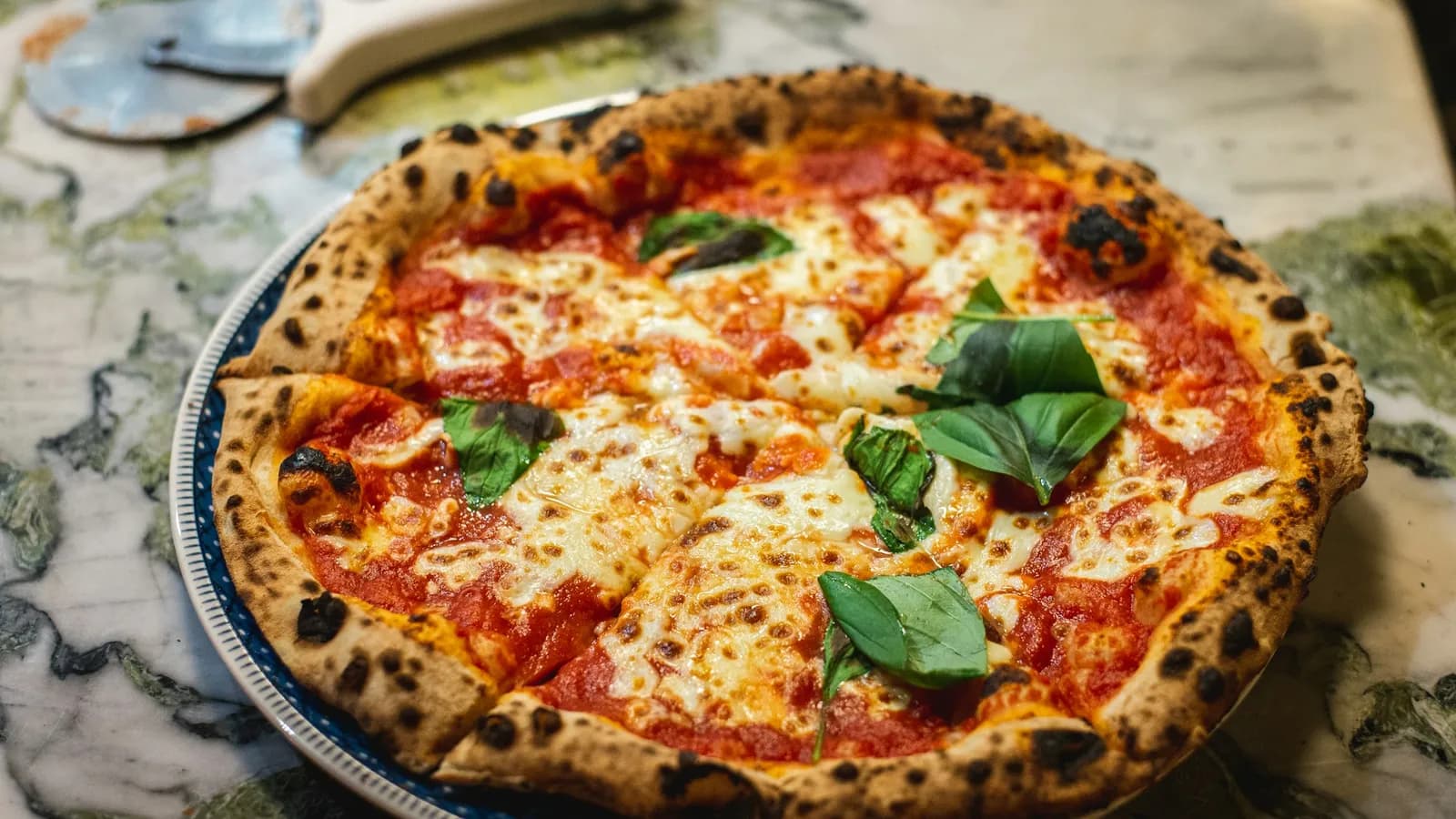Pizza margherita con albahaca fresca y cornicione moteado, recién salida del kamado