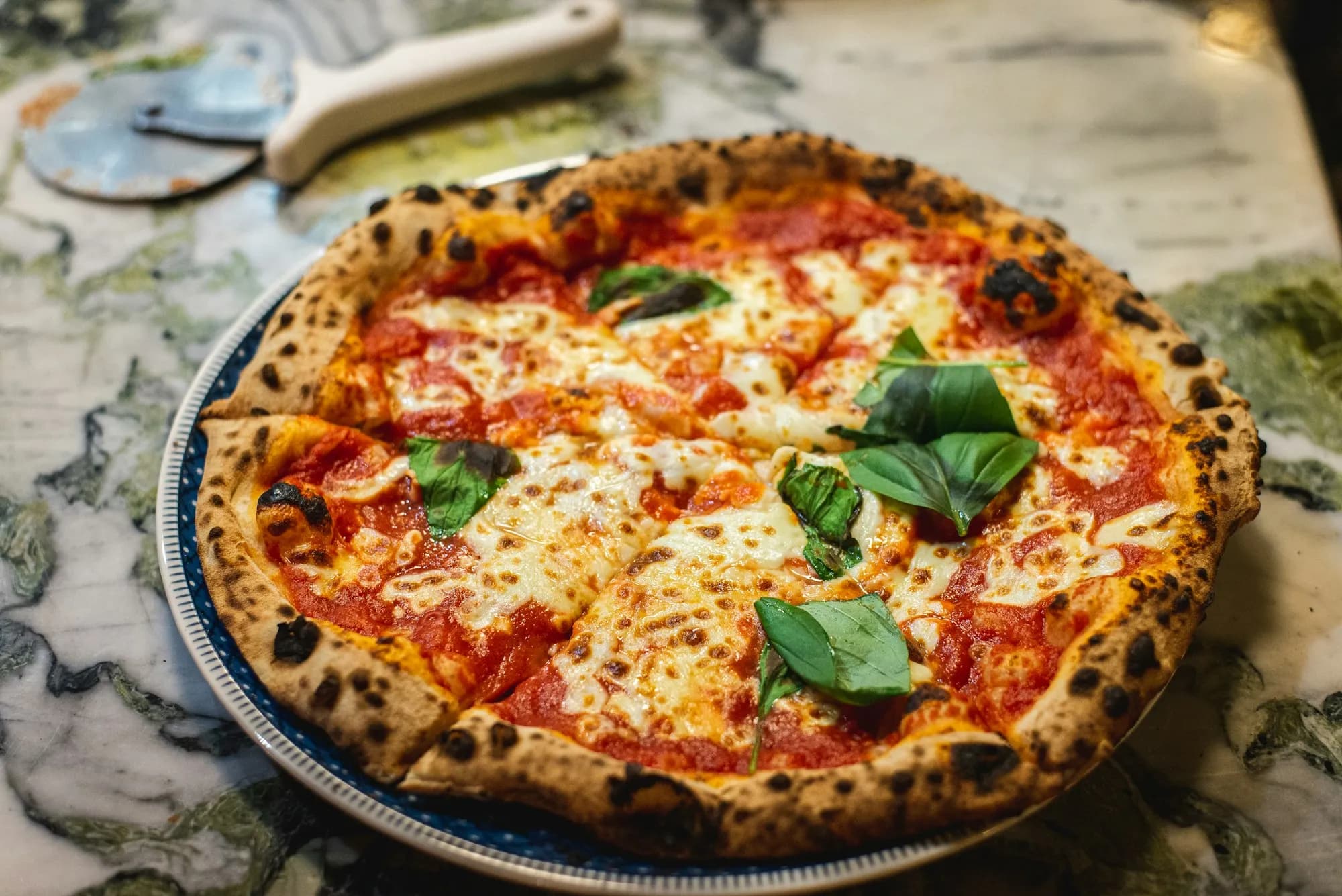 Pizza margherita con albahaca fresca y cornicione moteado, recién salida del kamado