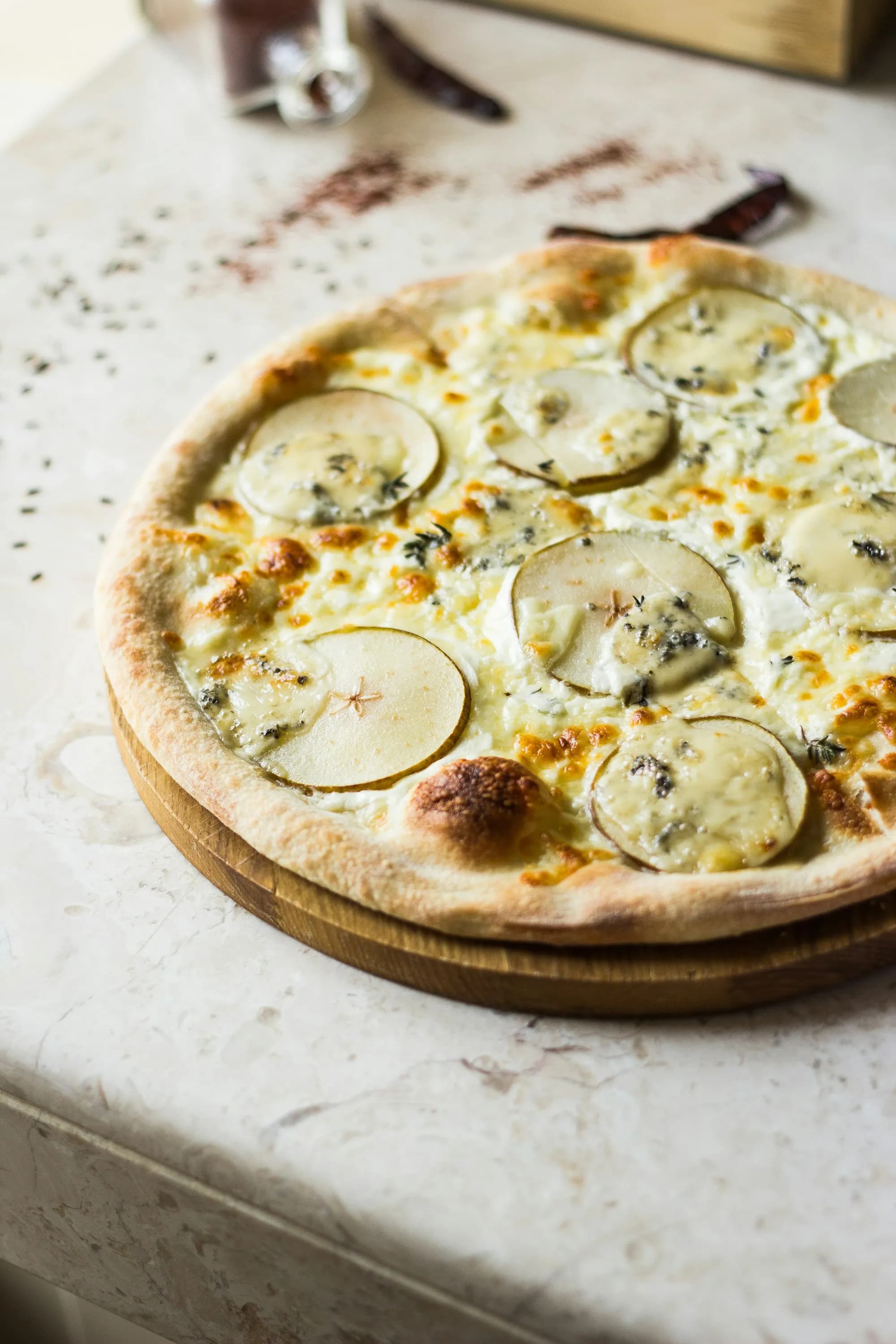Pizza quattro formaggi blanca con gorgonzola y láminas de pera sobre mármol