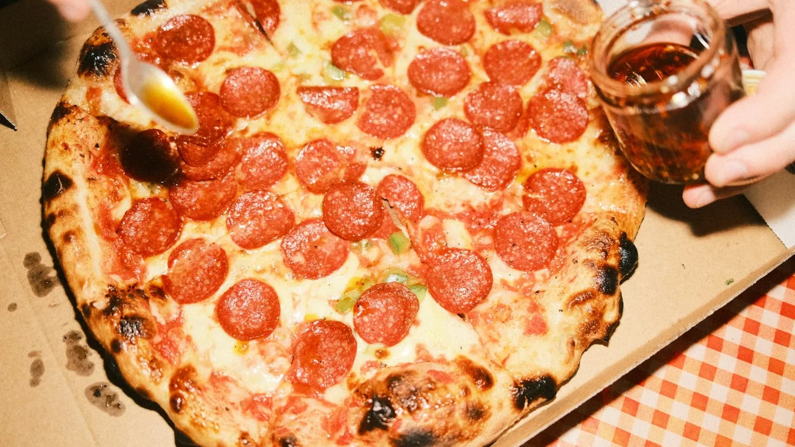 Pizza de embutido curado rojo con miel cayendo de una cuchara sobre la masa